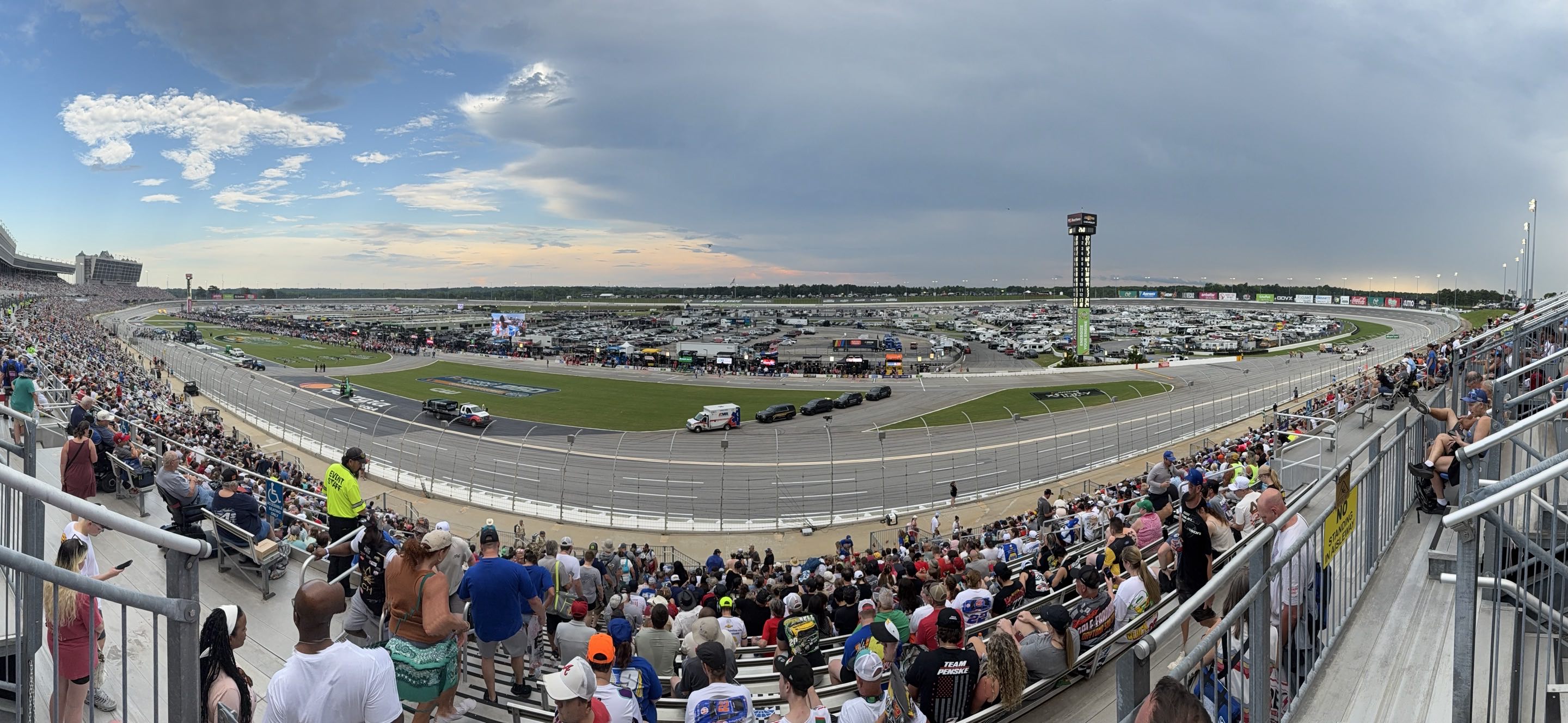 A spatially distorted panorama of an oval race track surrounded by crowded grandstands. An ominous cloud takes up half the sky.